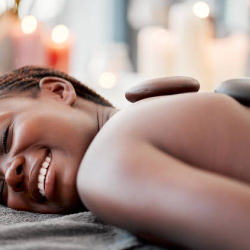 Hot stone massage, black woman at spa with smile on face, holistic healing with physical therapy and back skin detox. Happy, content and zen with wellness at luxury resort, rocks and relax with glow